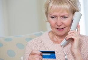 An elderly woman giving her credit card information to a scammer on the phone